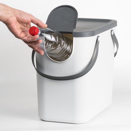 Hand deponeert een plastic fles in een witte afvalbak met een ronde opening.