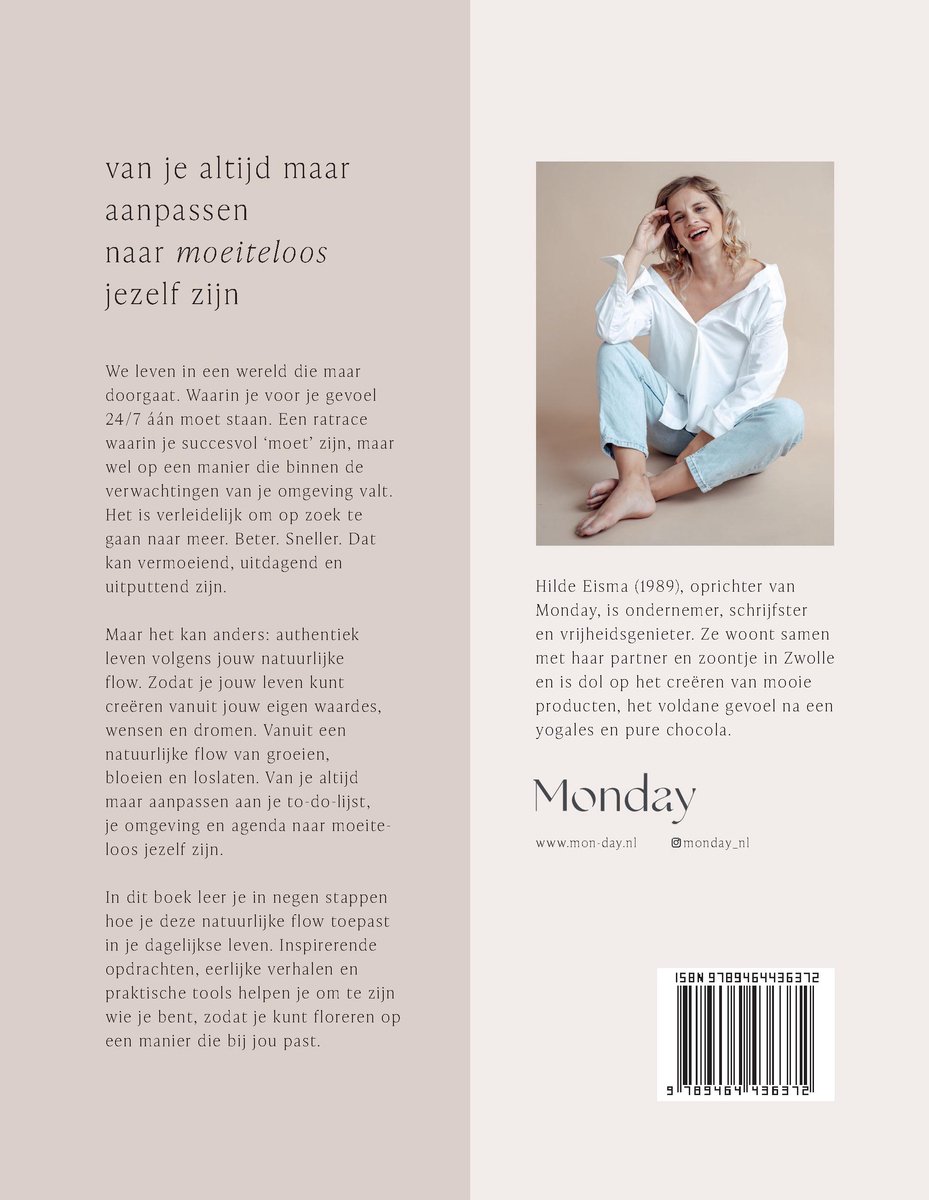 Vrouw in witte blouse en spijkerbroek, lachend, op blote voeten, met een beige achtergrond.
