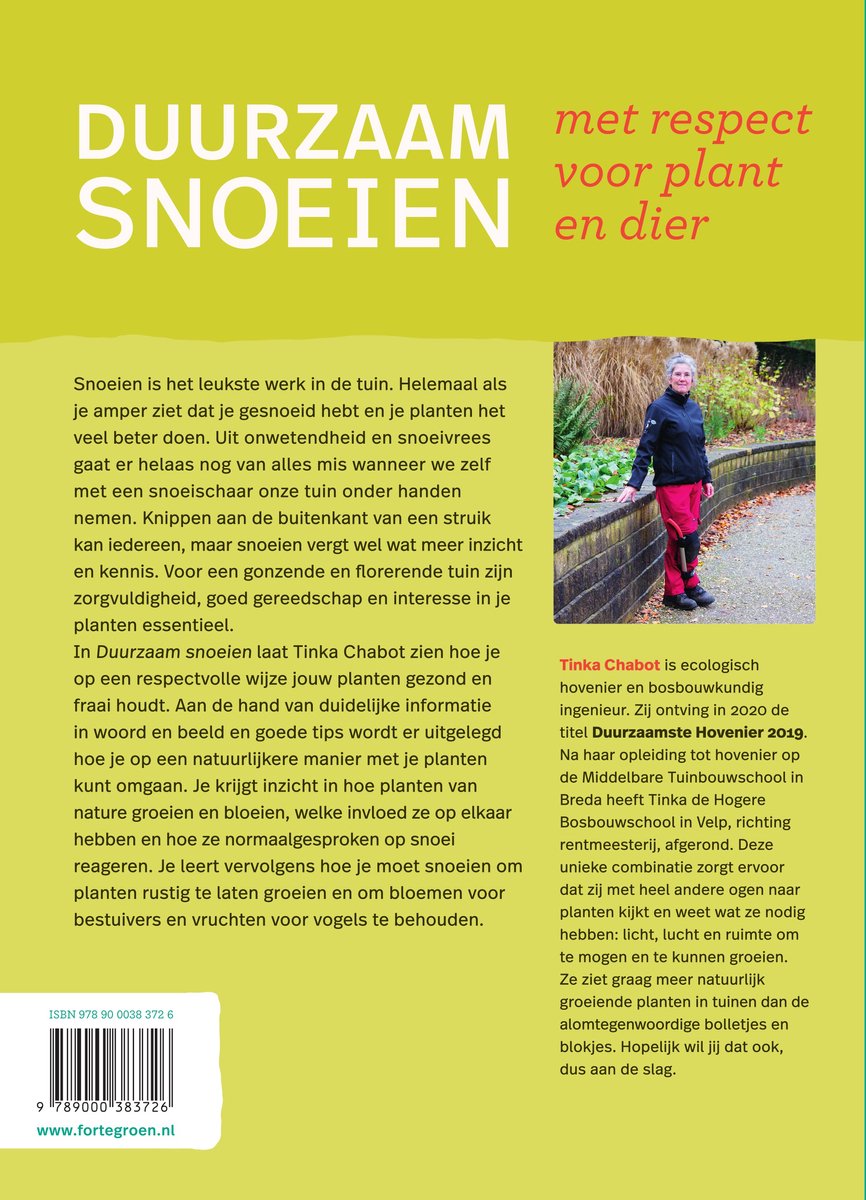Vrouw in groene jas en rode broek snoeit met snoeischaar in tuin.