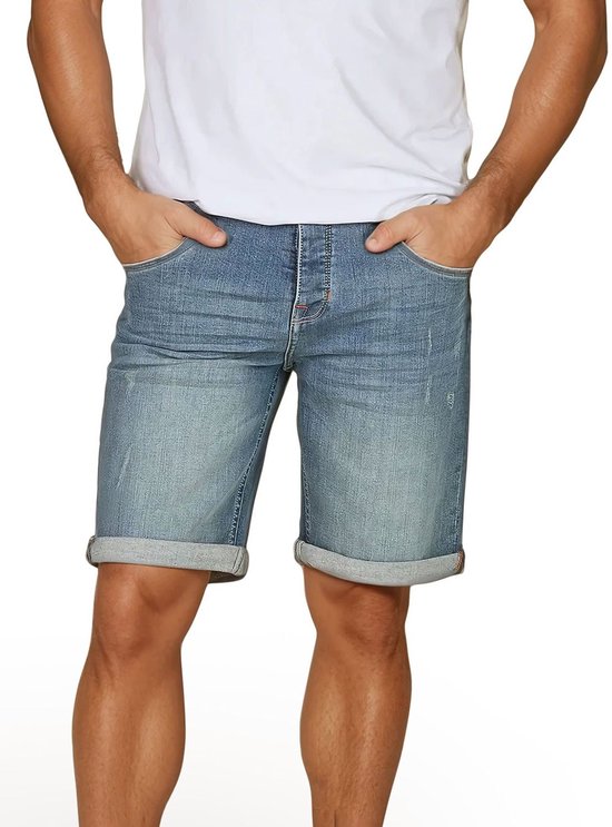 Man met handen in de zakken van een blauwe denim short, met omgeslagen broekspijpen.