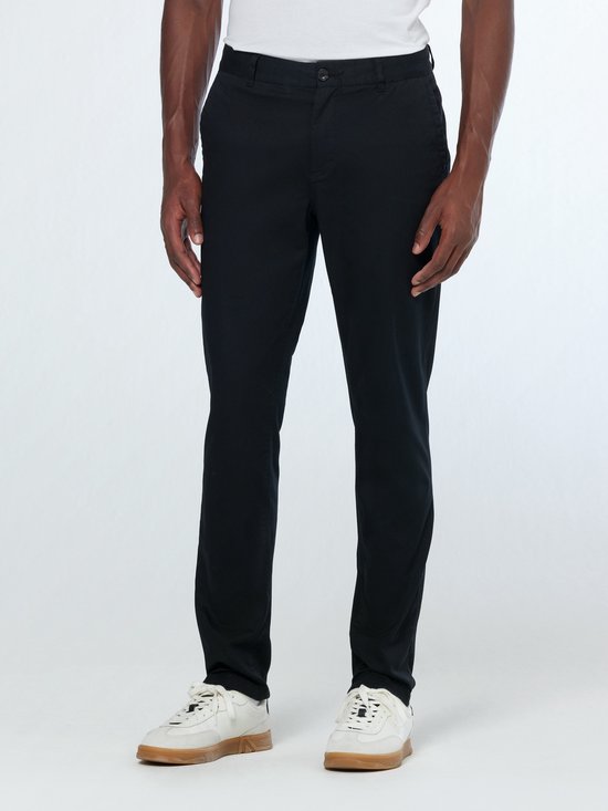 Mannequin portant un chino slim fit noir avec des baskets blanches. Taille boutonnée avec passants pour ceinture.