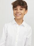 Gros plan d'un garçon souriant portant une chemise blanche.