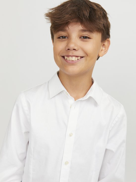 Gros plan d'un garçon souriant portant une chemise blanche.