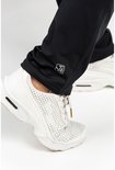 Detail van de onderkant van een zwarte trainingsbroek met het logo en witte sportschoenen.