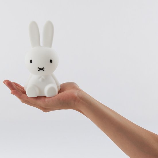 Hand houdt een wit Miffy-lampje met kruisjesmondje vast, met witte achtergrond.
