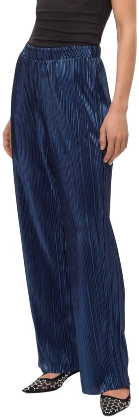 Model draagt een donkerblauwe, glanzende, geplooide broek met wijde pijpen.