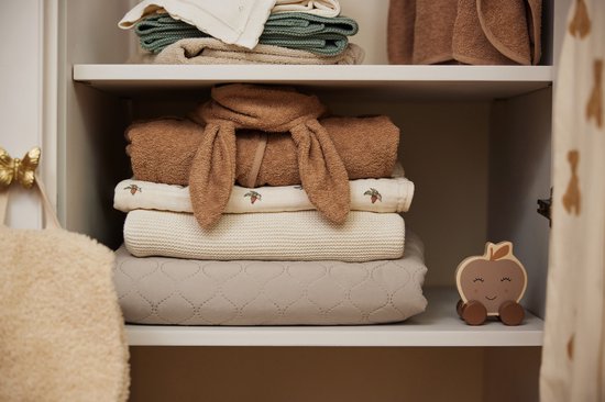 Couvertures de bébé empilées dans une armoire, avec une serviette marron aux oreilles de lapin par-dessus.