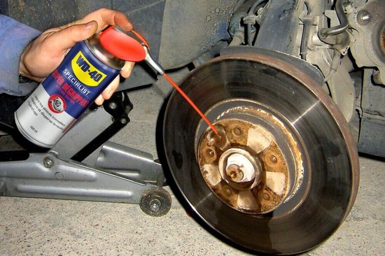 Man spuit WD-40 Specialist Super Kruipolie op een remschijf en naaf.