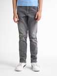 Jongen in een lichtblauwe T-shirt en grijze jeans, staand.