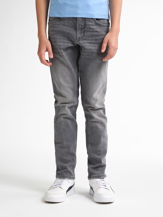 Jongen in een lichtblauwe T-shirt en grijze jeans, staand.