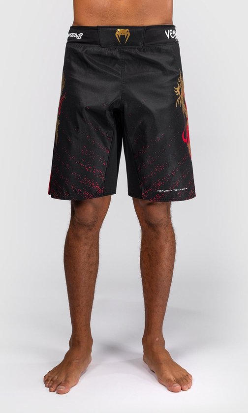 Voorkant van zwarte fightshorts met gouden draak, rode streep en rode spetters. Venum x Tekken 8 logo op de tailleband.