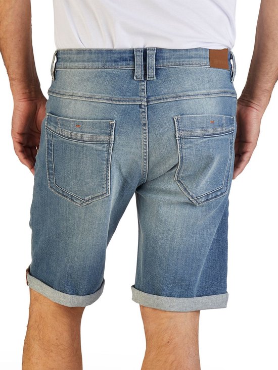 Achterkant, man draagt blauwe denim short met omgeslagen broekspijpen en Riverso-label.