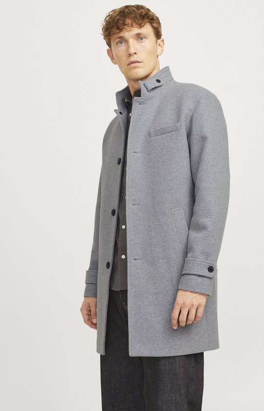 Model in grijze jas van wolmix met opstaande kraag en zwarte knopen, met donkere jeans.