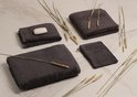 Trois serviettes gris foncé, un morceau de savon et des tiges de blé sur une surface en marbre.