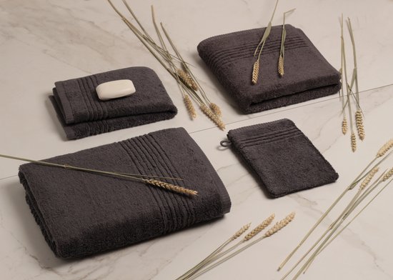 Trois serviettes gris foncé, un morceau de savon et des tiges de blé sur une surface en marbre.