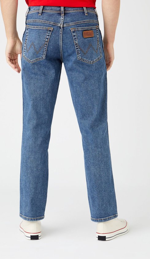 Man, staand, draagt een blauwe spijkerbroek, achterkant, met witte sneakers.