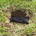 De zwarte, diervriendelijke mollenklem geplaatst in een gat in het gras, naast een molshoop.
