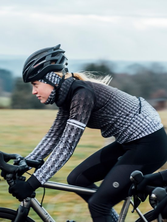 Vrouw op een fiets in een zwart fietsshirt met lange mouwen, een geometrisch grijs-wit patroon en witte strepen op de mouwen.