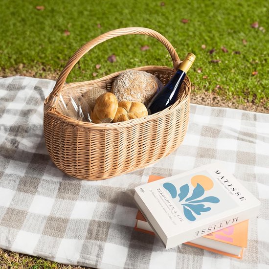 Panier en osier sur une couverture de pique-nique, rempli de petits pains, d'une bouteille de vin et de livres.
