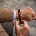Zwarte gevlochten lederen armband met kralen van zwarte lavasteen en mat zwart, gedragen om een mannenpols, met blazer.
