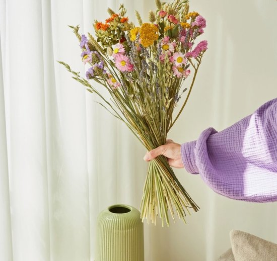 Hand houdt een boeket wilde bloemen vast in diverse kleuren: roze, paars, geel en oranje.