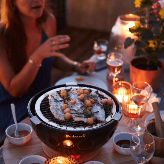 Zwarte tafelgrill met gegrilde vis en aardappeltjes, in sfeervol avondlicht.