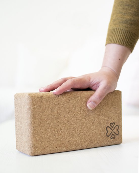 Hand van een vrouw rust op een kurken yogablok met klaver-hartlogo.