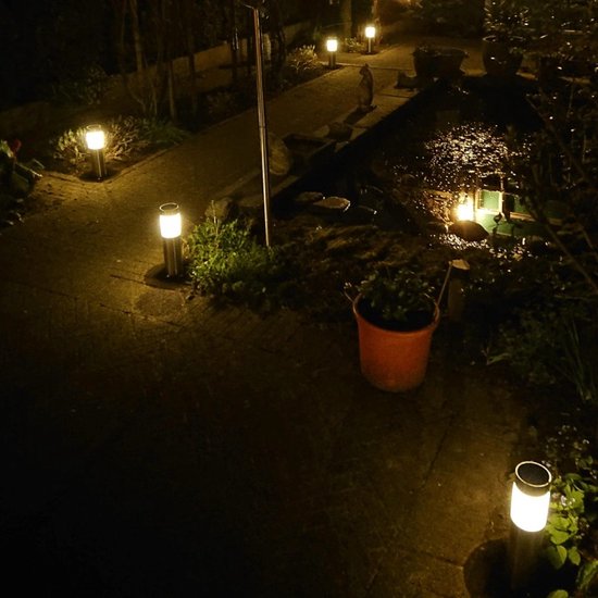 Zilverkleurige solar paaltjes met witte verlichting, langs een pad en vijver in de nacht.