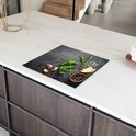 Zwarte inductiebeschermer met betonprint, bedekt met kruiden, knoflook, citroen en peperkorrels, op een marmeren aanrecht.