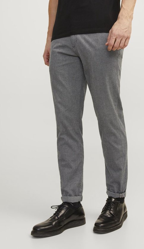 Model in grijze broek met subtiel visgraatpatroon, zwarte schoenen en sokken.