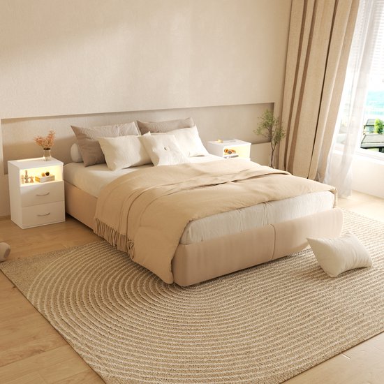 Slaapkamer met wit bed, zandkleurige deken, rond vloerkleed en twee witte nachtkastjes met verlichting.