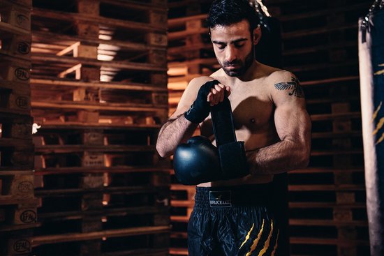 Een man met bokshandschoenen en bandageert zijn pols in een gymzaal.