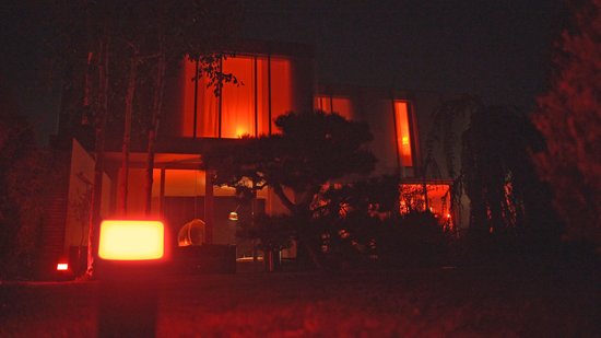 Moderne villa 's nachts met rode sfeerverlichting buiten, een verlichte lamp en veel ramen.
