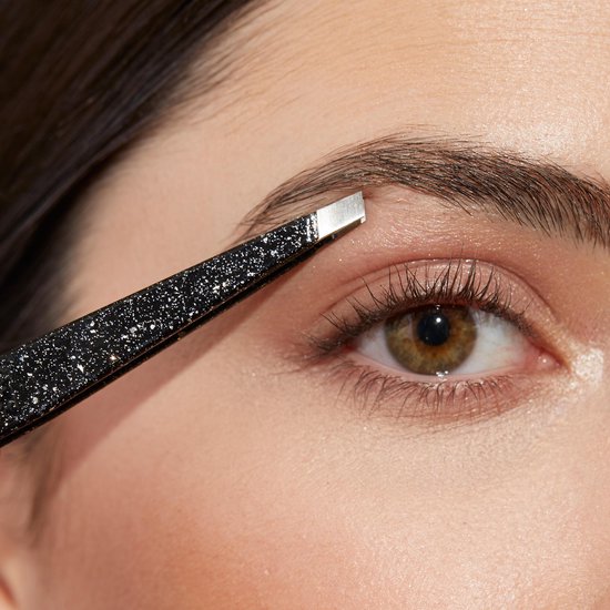 Close-up van een vrouwenoog en wenkbrauw waarbij een zwarte glitter pincet wordt gebruikt.