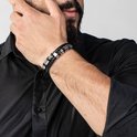 Gevlochten zwarte armband met zilverkleurige kralen en buisjes, gedragen door een man in zwart overhemd.