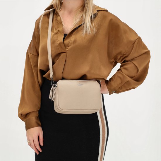 Een beige crossbody tas met franjes, gedragen door een model met een bruine blouse en zwarte rok.
