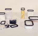 Set van transparante Mepal voorraadbakken met zwarte deksels, gevuld met witte bonen, zwarte bonen, rijst, chips en meer.