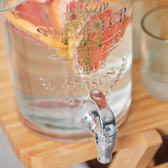 Close-up van een glazen drankdispenser met 'Hello Summer' opdruk, gevuld met water en partjes grapefruit.