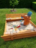 Jongetje speelt in een houten zandbak met banken en speelgoed.