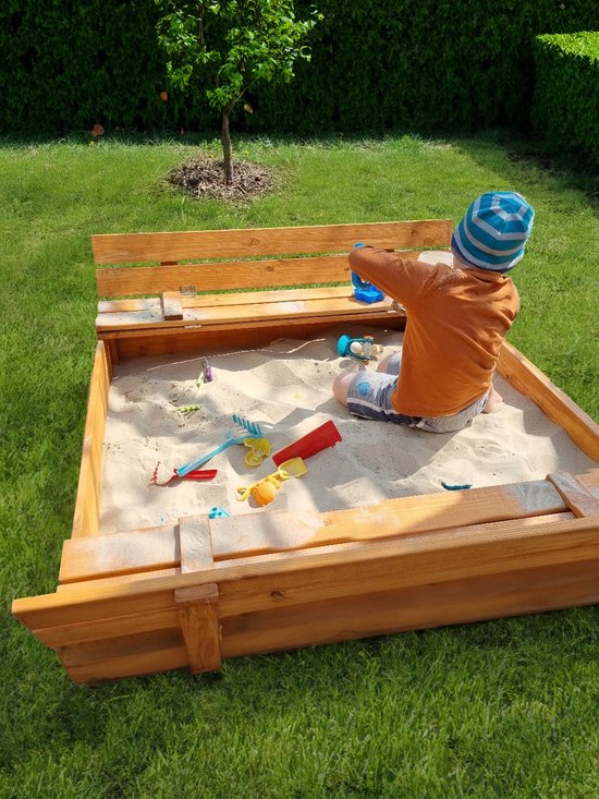 Jongetje speelt in een houten zandbak met banken en speelgoed.