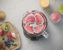 Bovenaf: Philips blender met draaiende rode smoothie. Fruit en glazen smoothies op tafel.