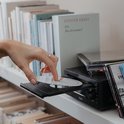 Hand steekt een CD in de lade van een zwart micro-stereosysteem tussen boeken.