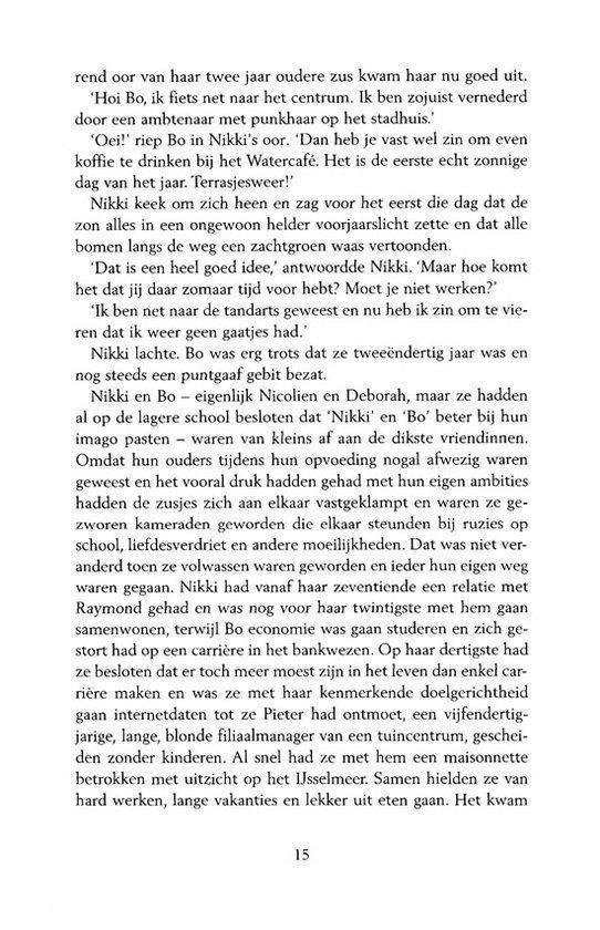 Een vrouw met lang blond haar en een roze blouse, zit aan een tafel in een café.