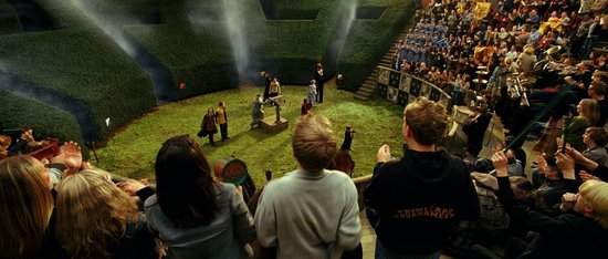 Studenten kijken naar een toernooi in een doolhof van hagen, met een menigte op de tribunes.