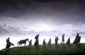 Silhouetten van een groep figuren, waaronder een ruiter te paard, die over een heuveltop lopen met bergen op de achtergrond.