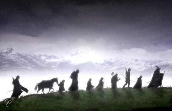 Silhouetten van een groep figuren, waaronder een ruiter te paard, die over een heuveltop lopen met bergen op de achtergrond.