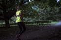 Vrouw in het donker joggend met een fluoriserend geel hesje met reflecterende strepen.