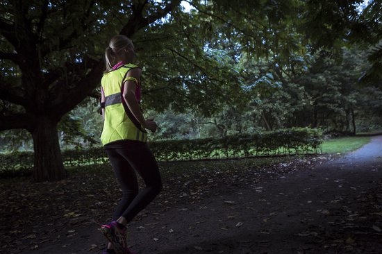 Vrouw in het donker joggend met een fluoriserend geel hesje met reflecterende strepen.