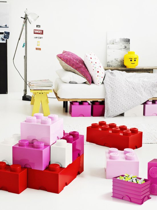 Een kinderkamer met een bed, speelgoed in felle kleuren, waaronder roze en rode Lego-opbergdozen.