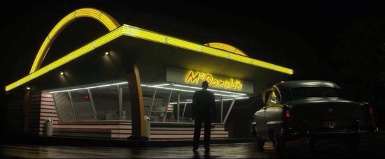 McDonald's restaurant 's nachts met gele bogen en verlichting. Een man staat voor het restaurant naast een auto.